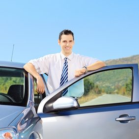 Smiling young male with tie posing next to his automobile on an open road